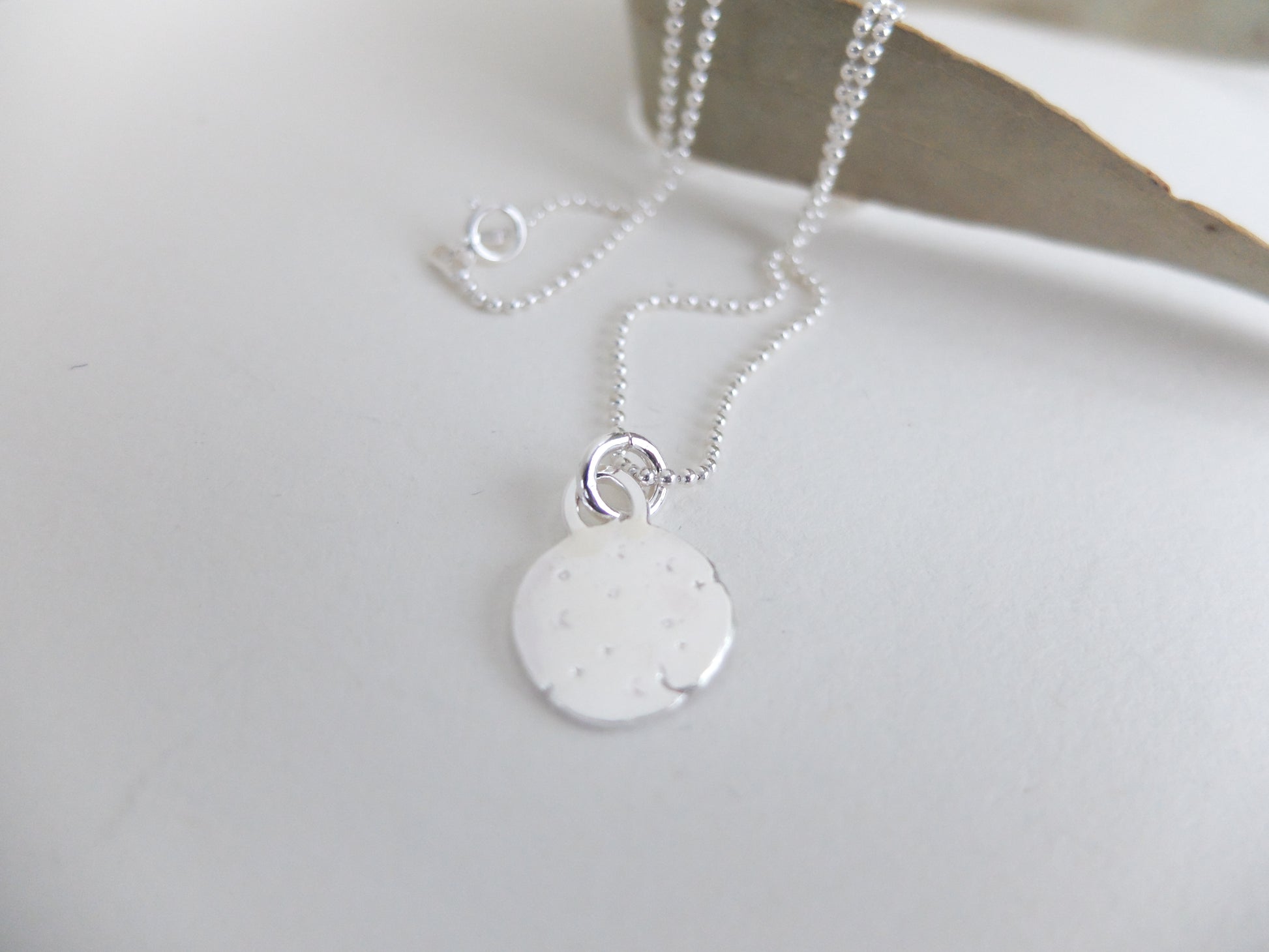 Silver necklace with a round pendant on a white surface