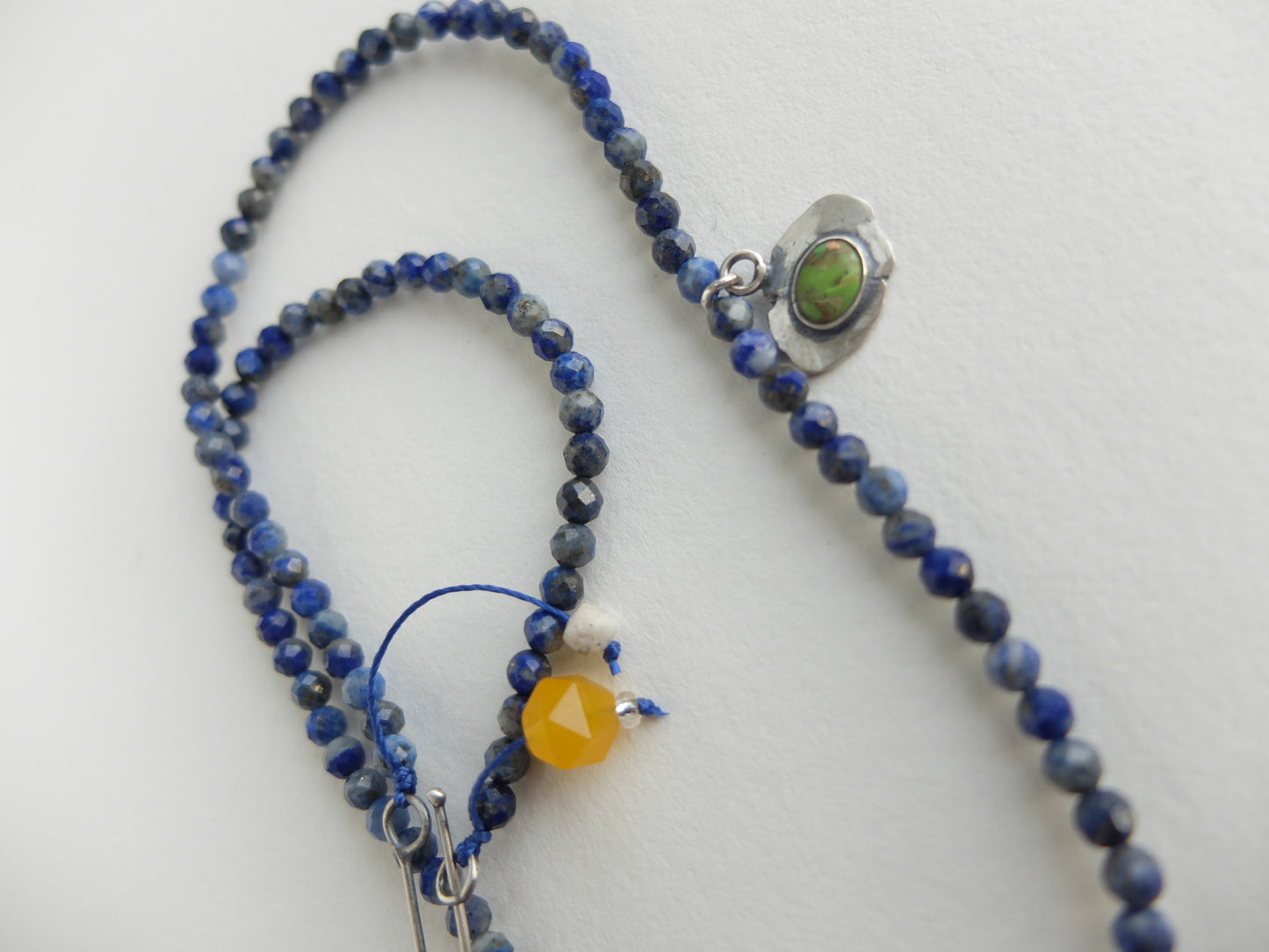 Necklace with blue beads and a green stone pendant on a white background