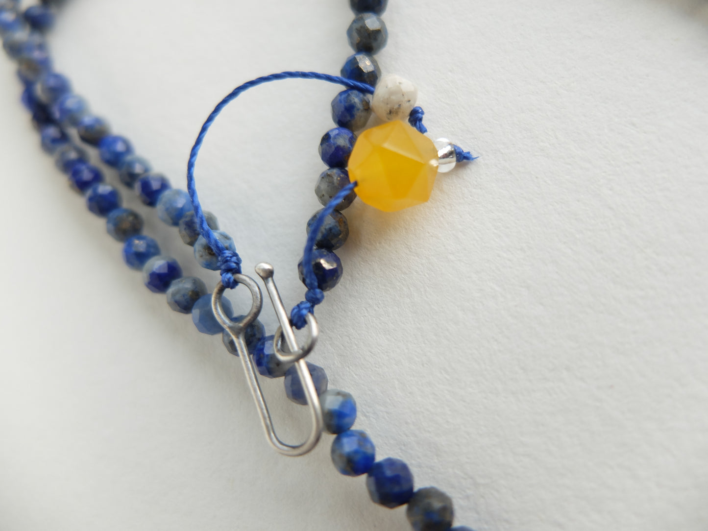 Close-up of a beaded necklace with blue and gray beads and a yellow accent bead on a white background.