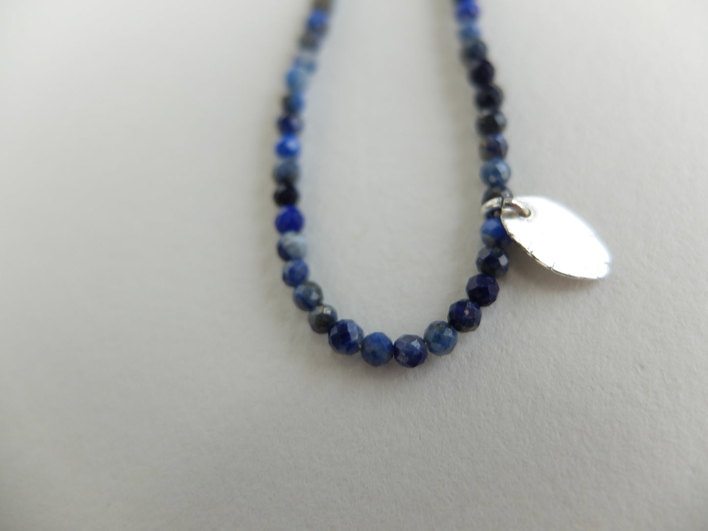 Blue beaded necklace with a silver tag on a white background