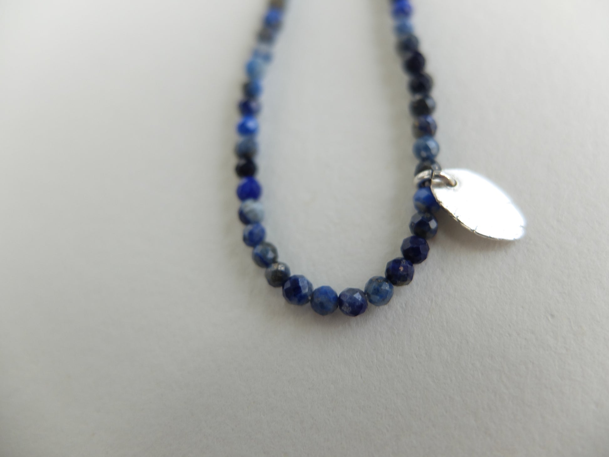 Blue beaded necklace with a silver tag on a white background
