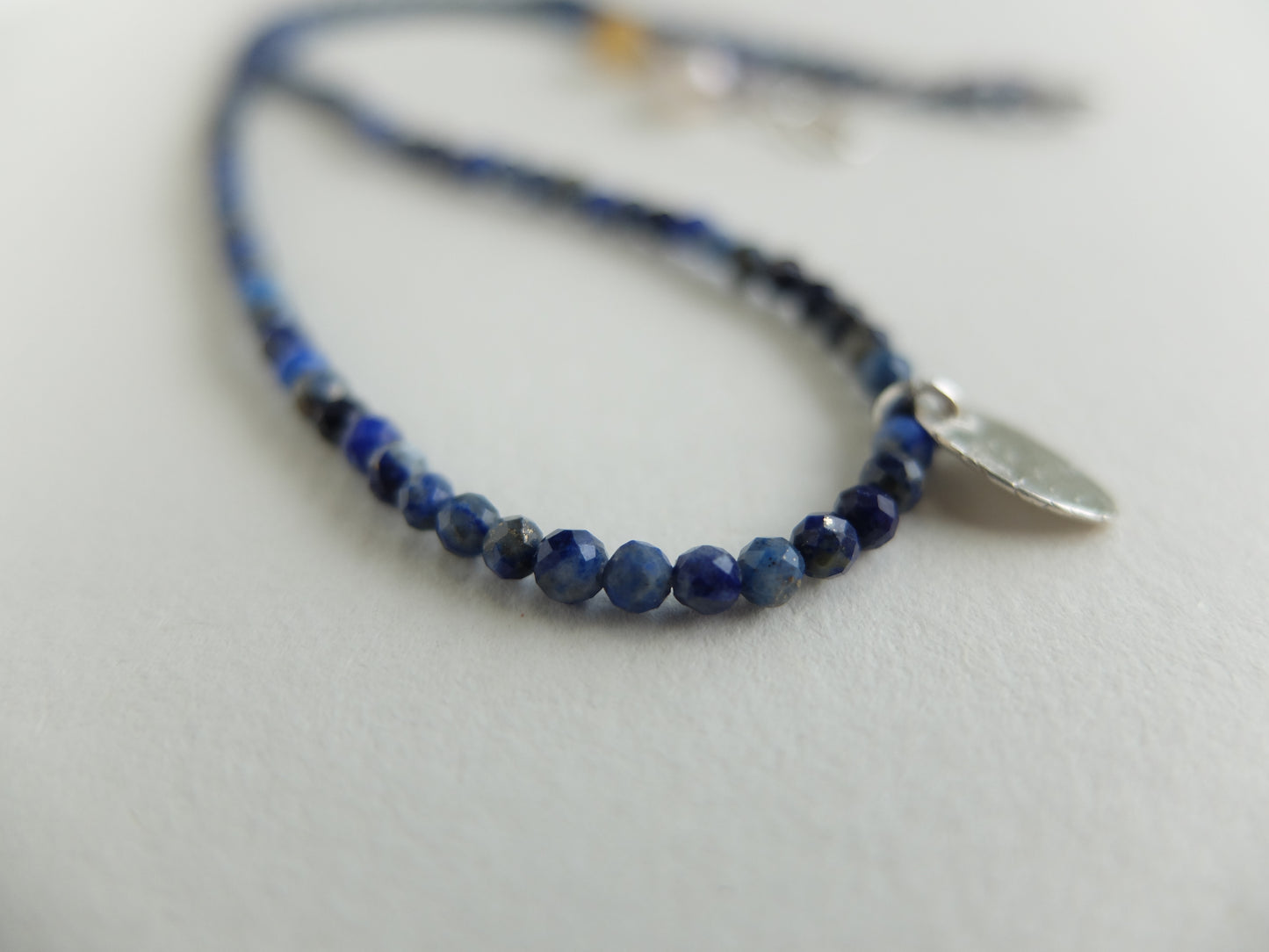 Blue beaded necklace with a silver tag on a light gray background