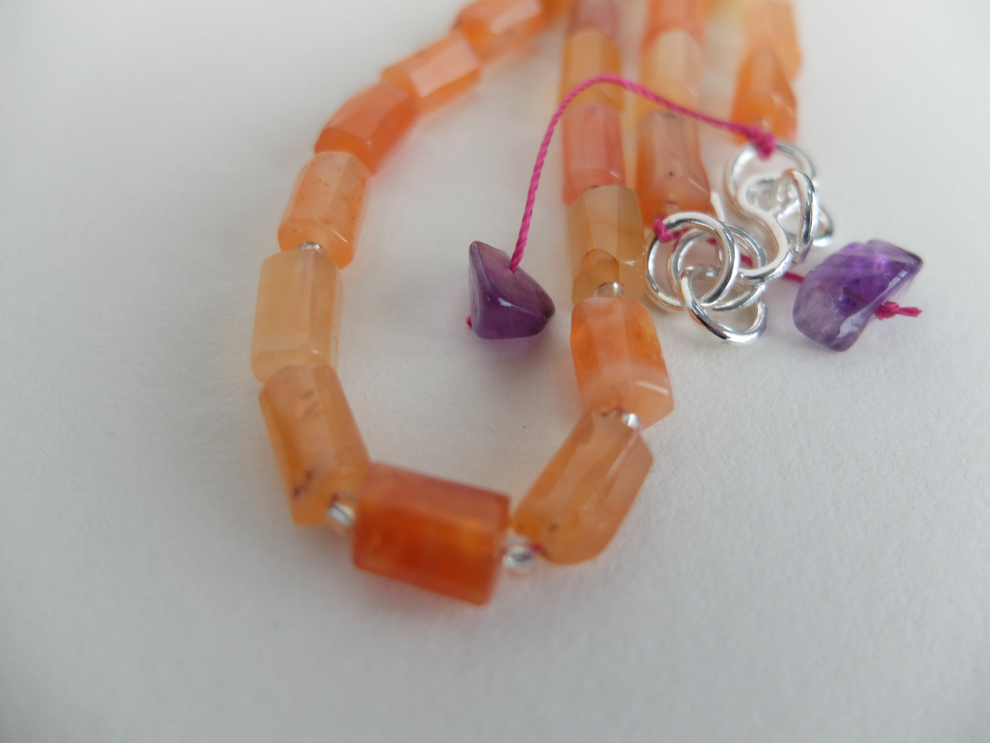 Orange beaded bracelet with silver and purple heart charms on a white background
