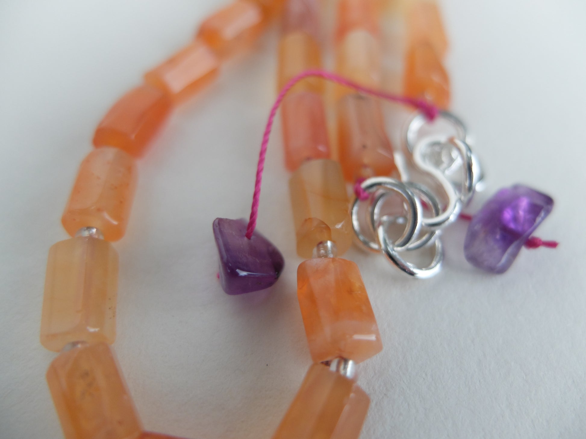 Necklace with orange beads and purple and silver charms on a white background